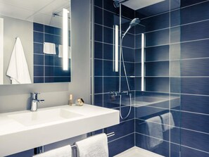 Un baño moderno con un espejo grande, un lavamanos blanco, un cabezal de ducha de mano y paredes cubiertas de azulejos azul oscuro.