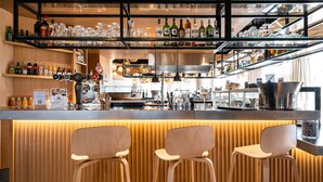 A bar area with wooden stools, shelves of bottles, and a kitchen in the background. - Mercure Compiegne Sud (Lacroix-Saint-Ouen)