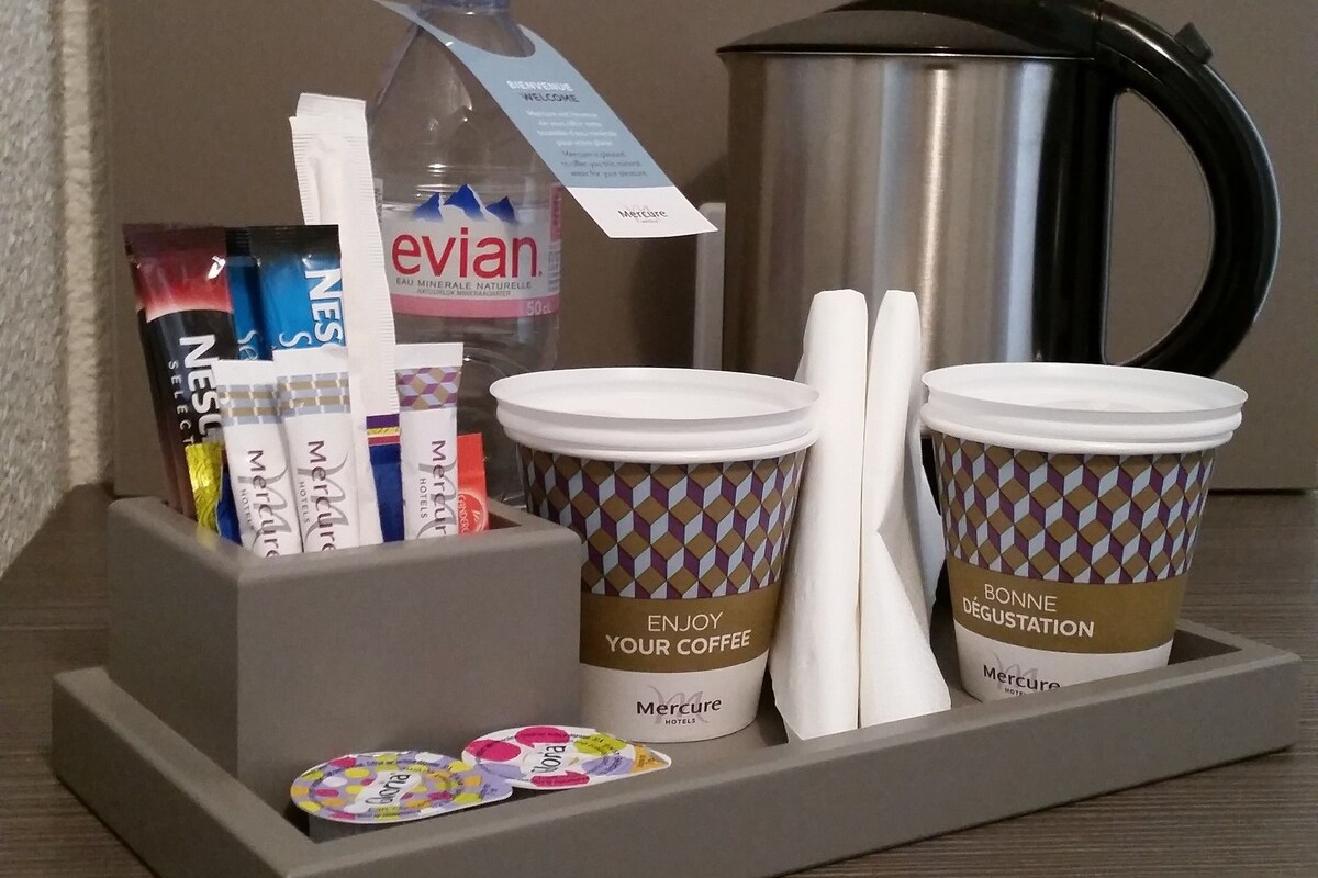 A hotel room's coffee station with disposable cups, a kettle, and various toiletries.