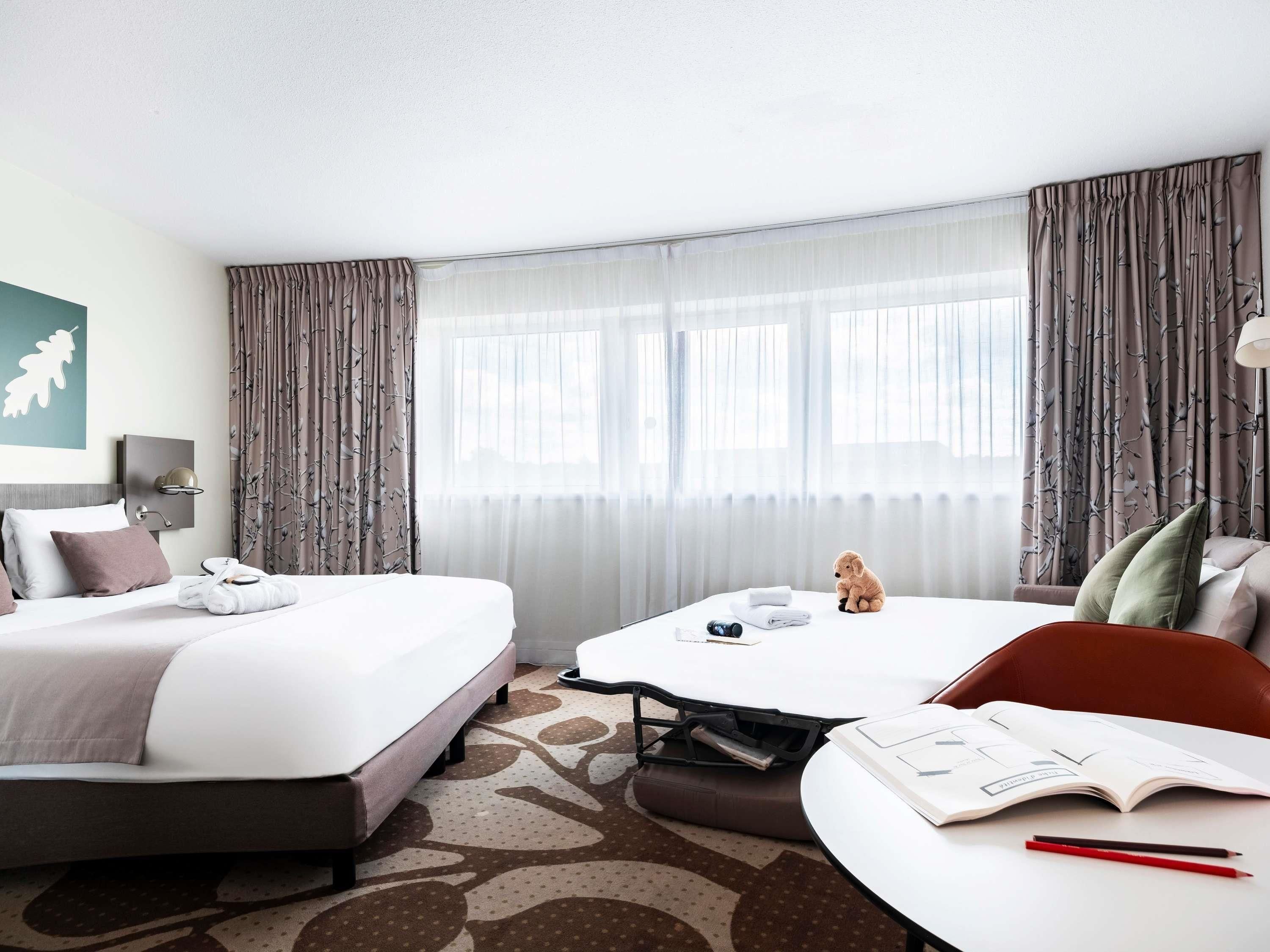 Habitación de hotel con cama, escritorio, silla y ventana con cortinas.