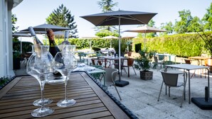 An outdoor patio with wooden tables, clear glasses, and bottles, surrounded by umbrellas and chairs. - Mercure Compiegne Sud (Lacroix-Saint-Ouen)