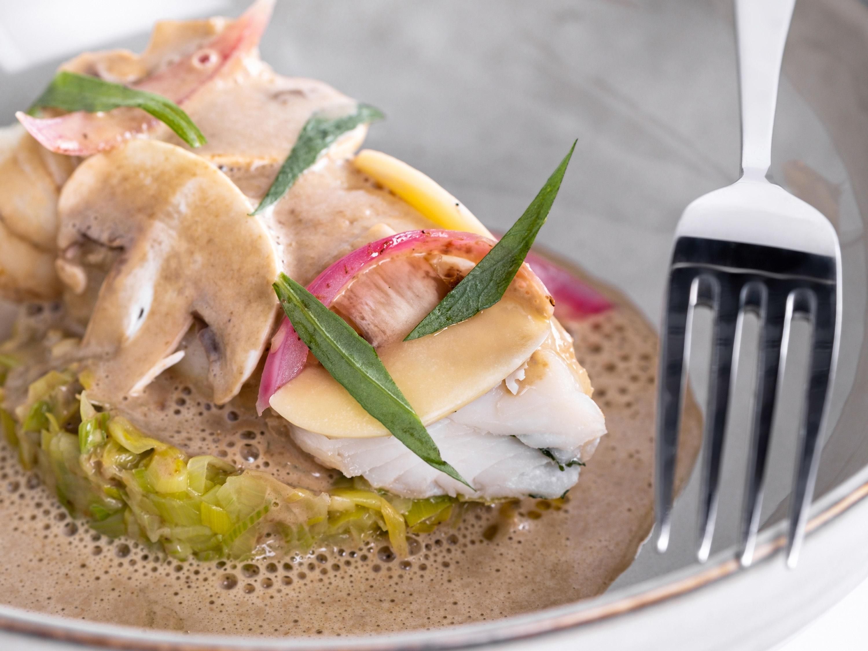 A dish with fish, vegetables, and a foam-like sauce on a plate.