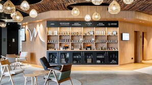 A modern interior with a wooden reception desk, shelves with various products, and a seating area with chairs and a table. - Mercure Compiegne Sud (Lacroix-Saint-Ouen)