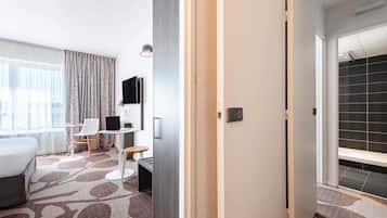 Una camera d'hotel con un letto, una scrivania con un portatile, una sedia, una TV e una finestra con tende.