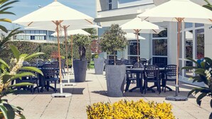 An outdoor seating area with tables and chairs, umbrellas, and potted plants. - Mercure Compiegne Sud (Lacroix-Saint-Ouen)