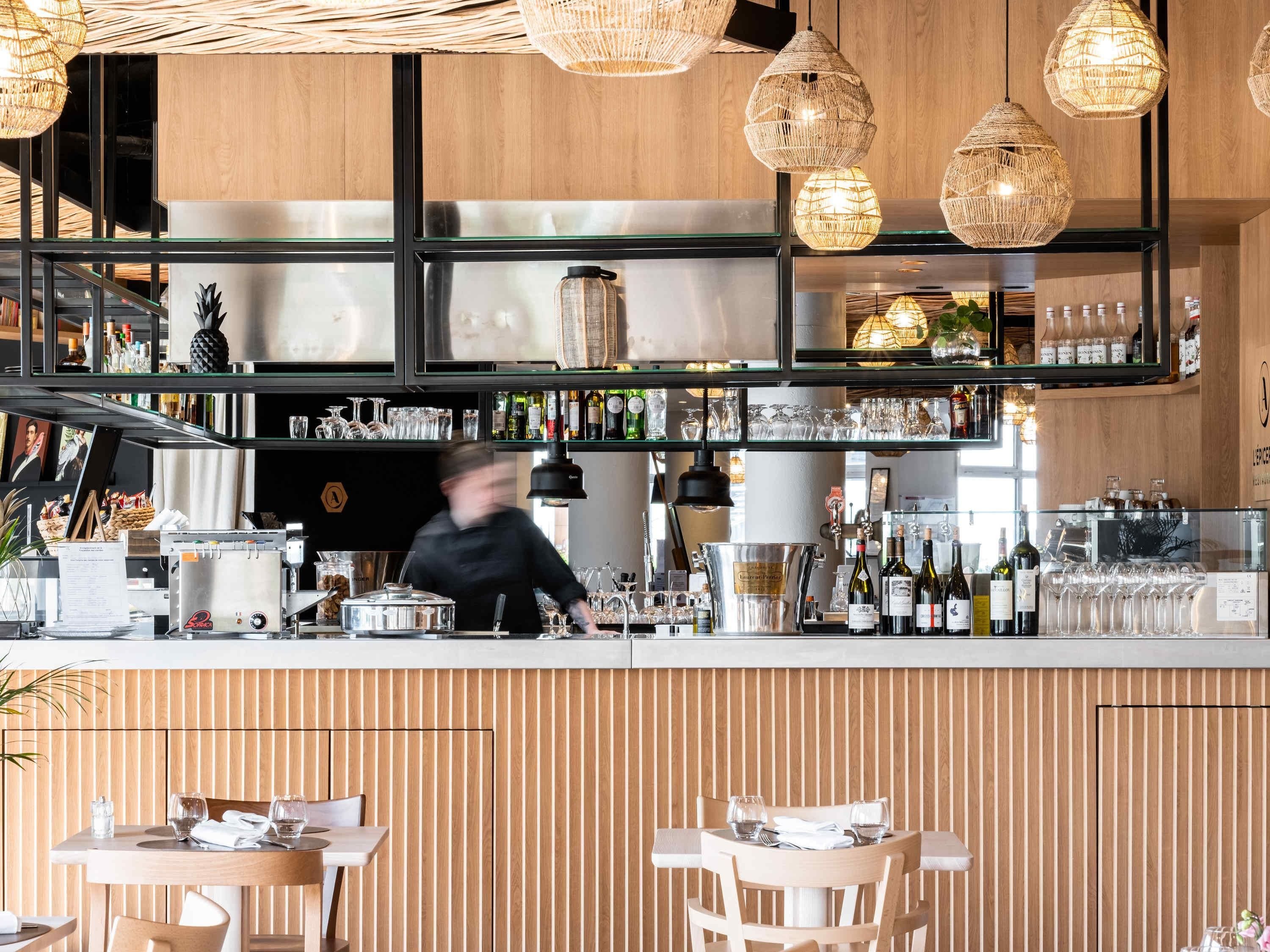 A modern bar area with wooden paneling, hanging wicker lights, and a variety of bottles and glasses on shelves.
