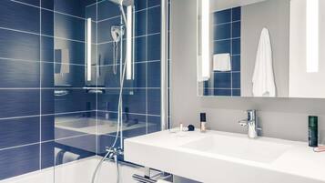 Une salle de bain moderne avec une douche à parois de verre, un lavabo blanc et un grand miroir.