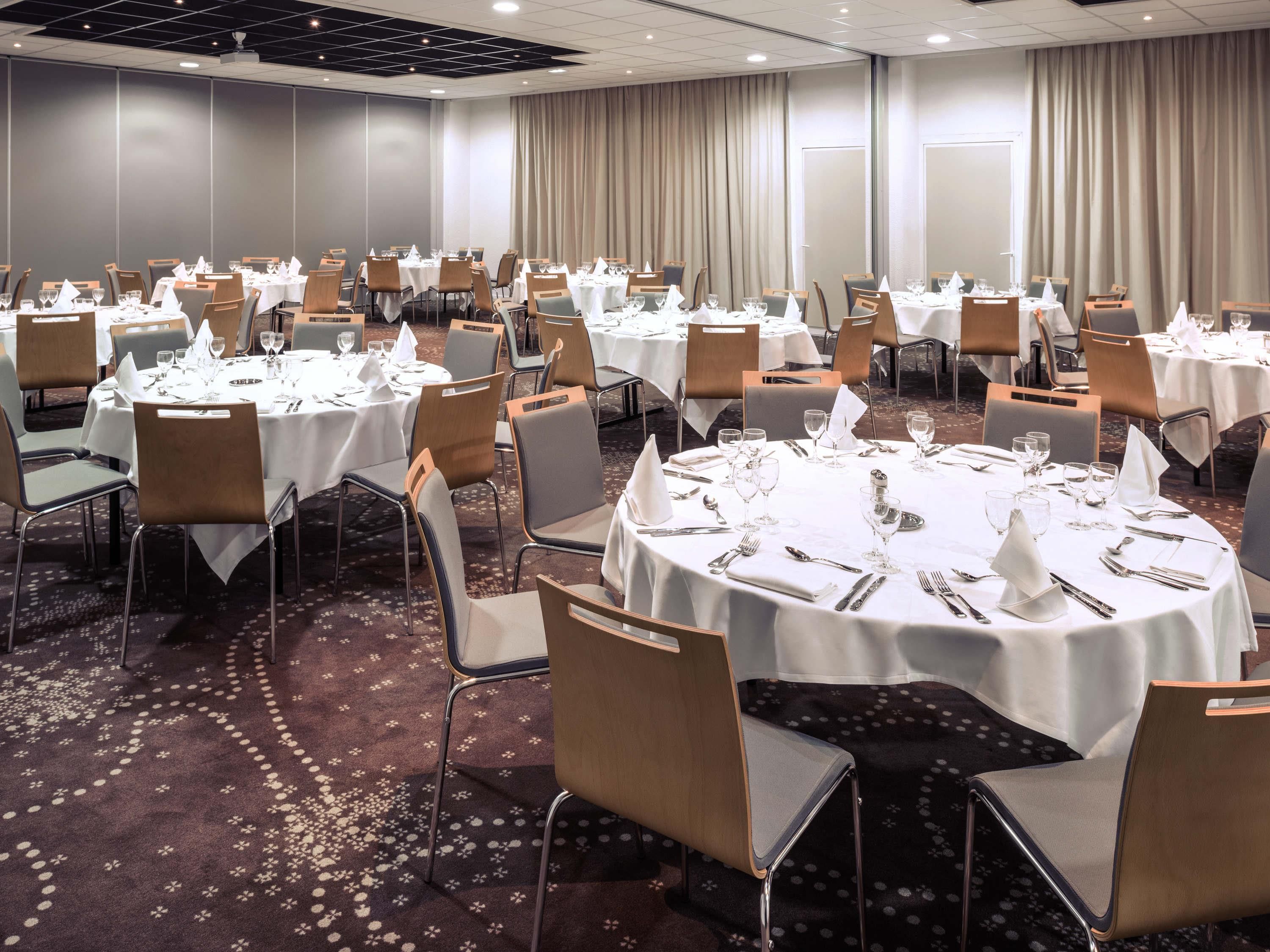 A conference room with round tables, chairs, and a carpeted floor.