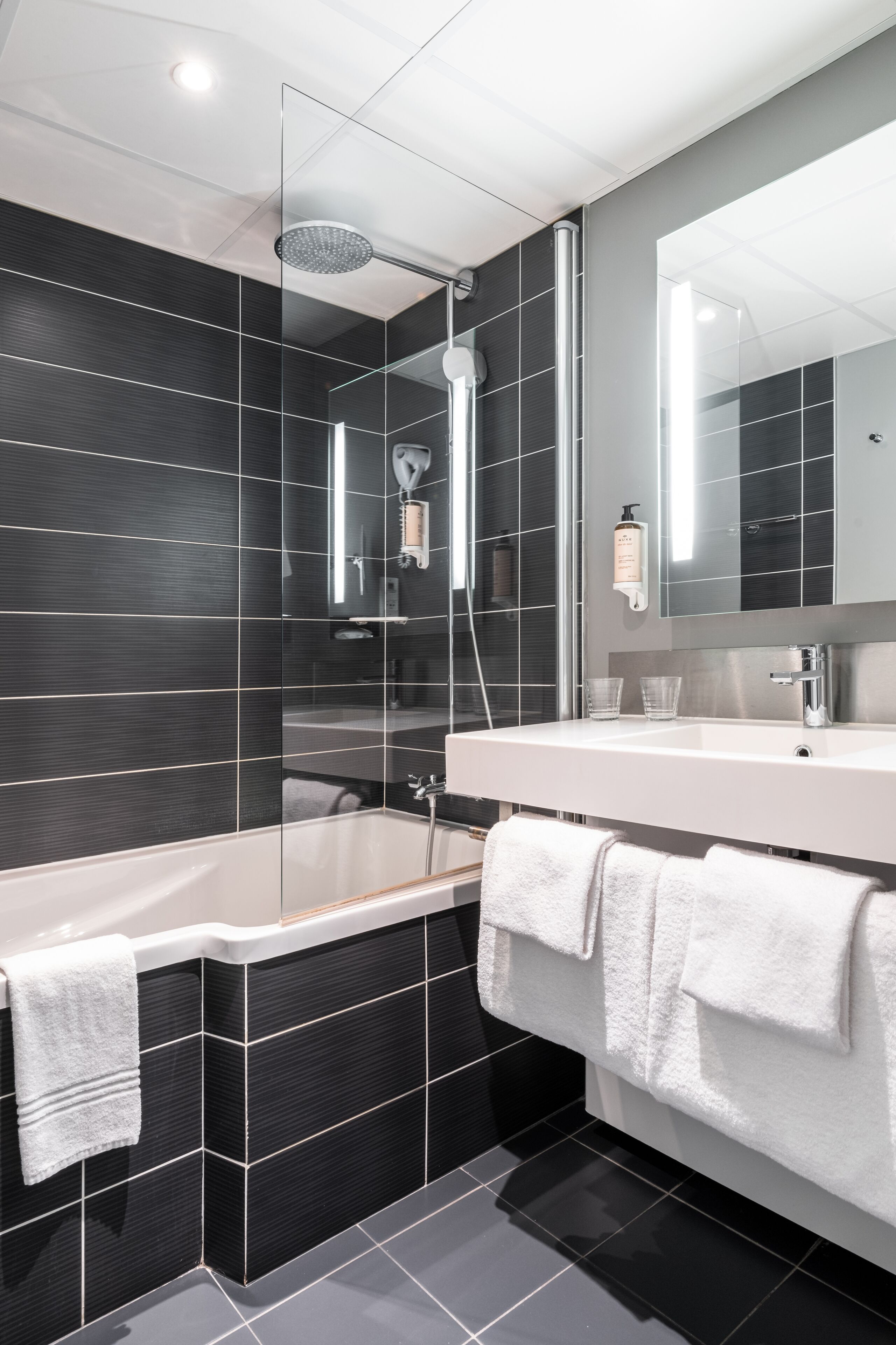 A modern bathroom with a glass-enclosed shower, a white bathtub, and a large mirror above the sink.