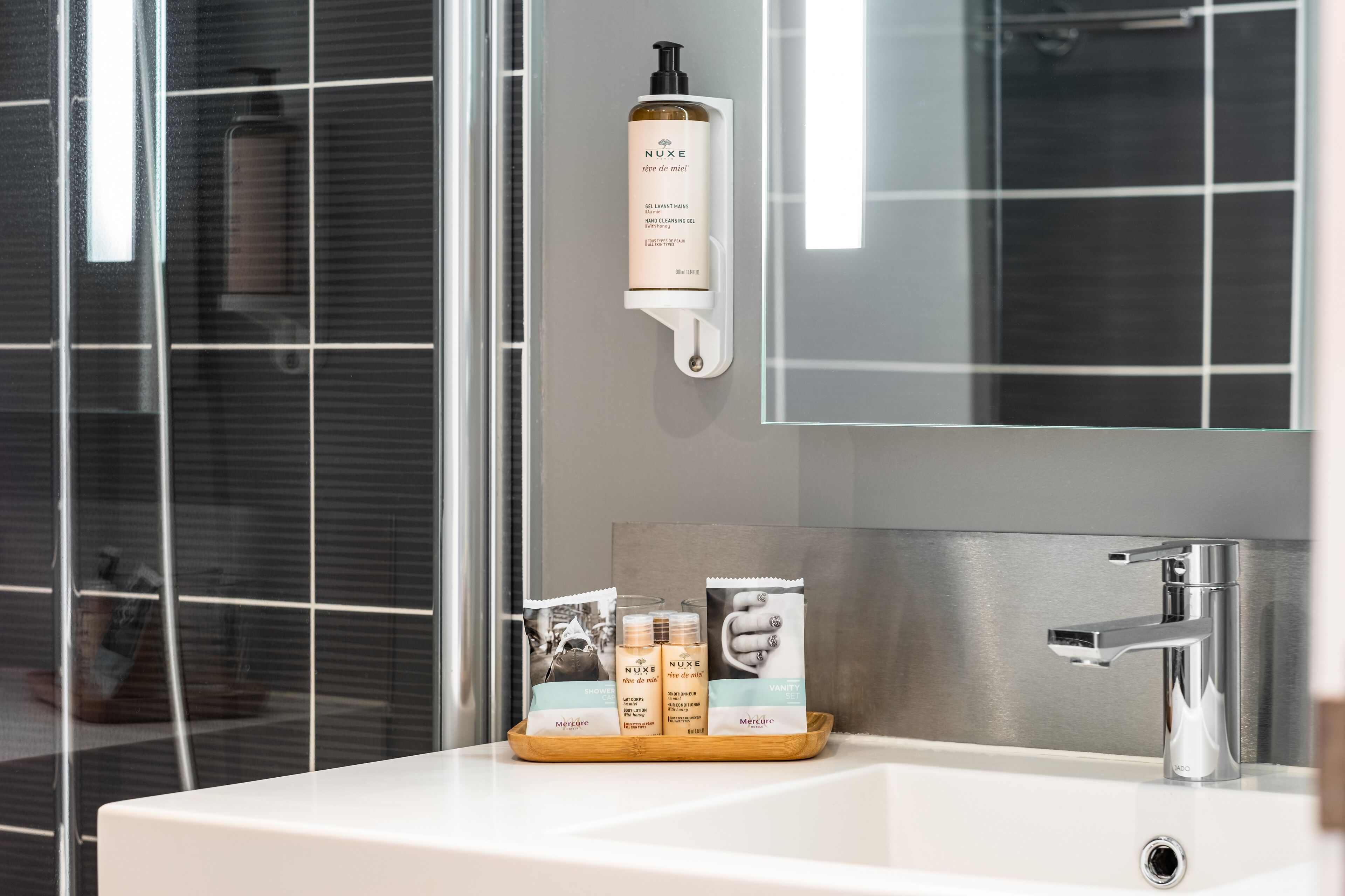 A bathroom with a white sink, a mirror, and a hand soap dispenser mounted on the wall.