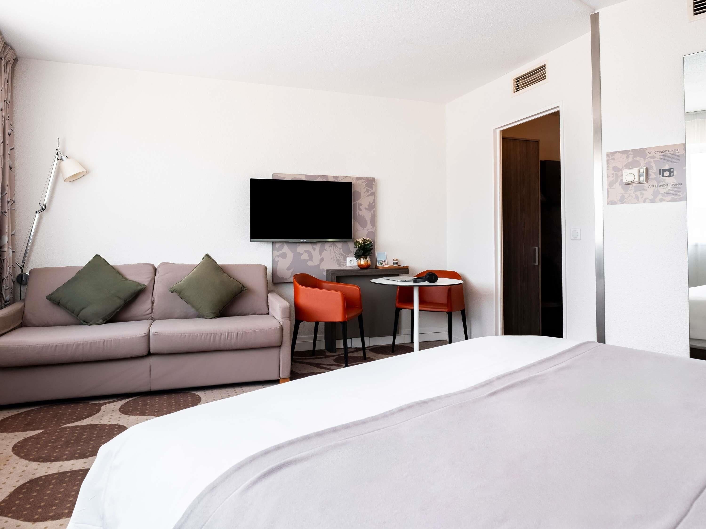 Habitación de hotel con cama, sofá, escritorio y dos sillas, televisor de pantalla plana y puerta.