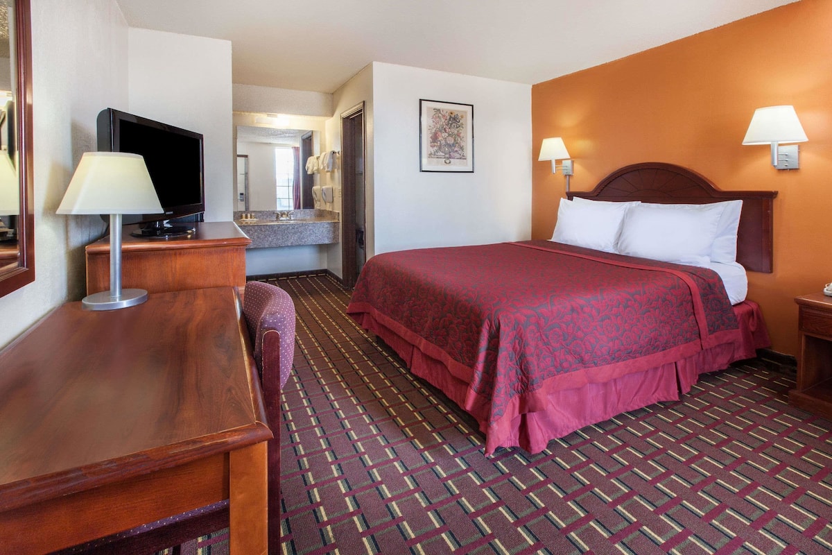 A hotel room with a bed, a television, a desk, a mirror, and a bathroom visible in the background.