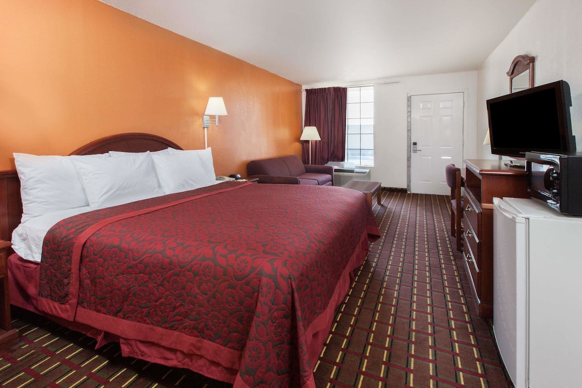 A hotel room with a large bed, a desk with a television, a chair, and a window with curtains.