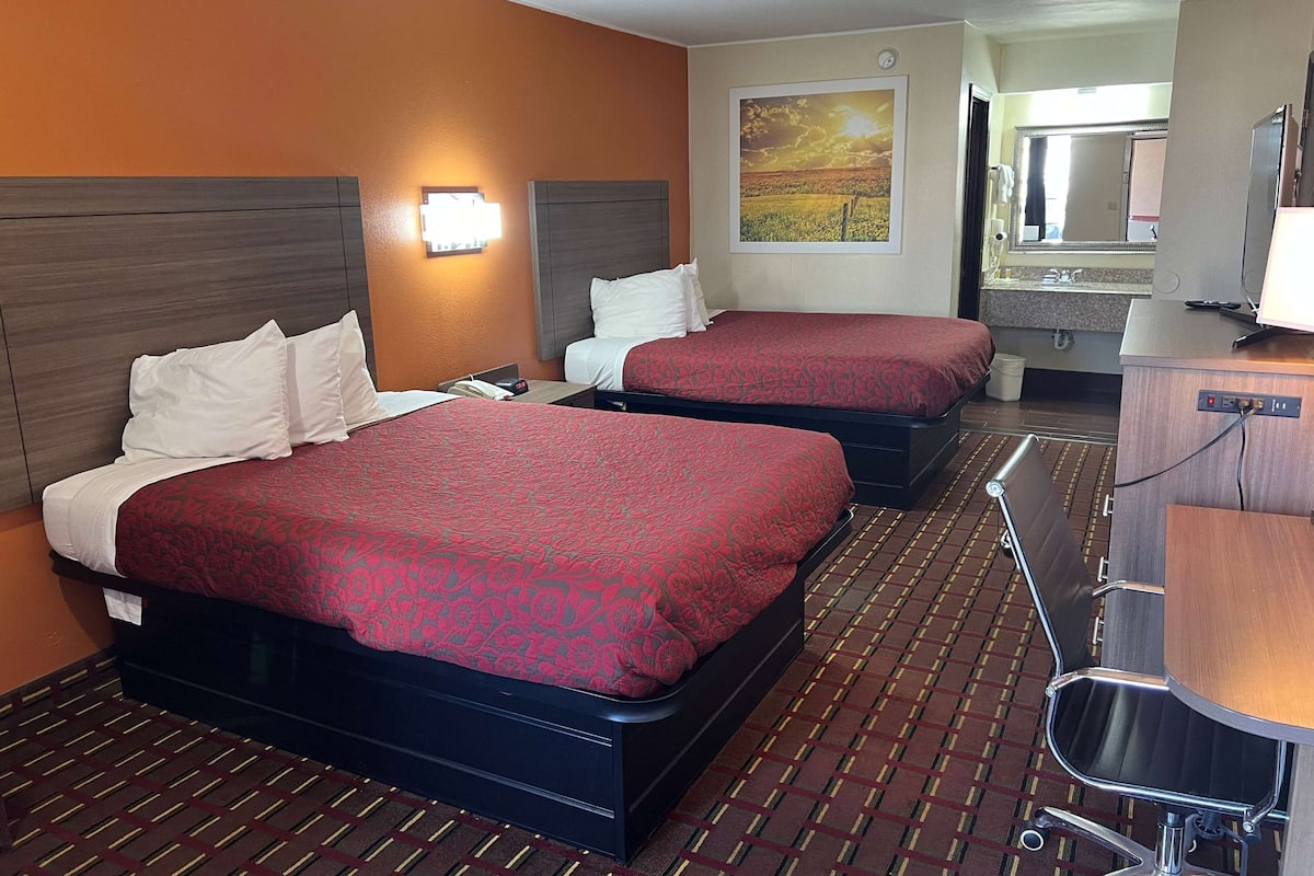 A hotel room with two beds, a desk, a chair, a mirror, and a bathroom visible through an open door.