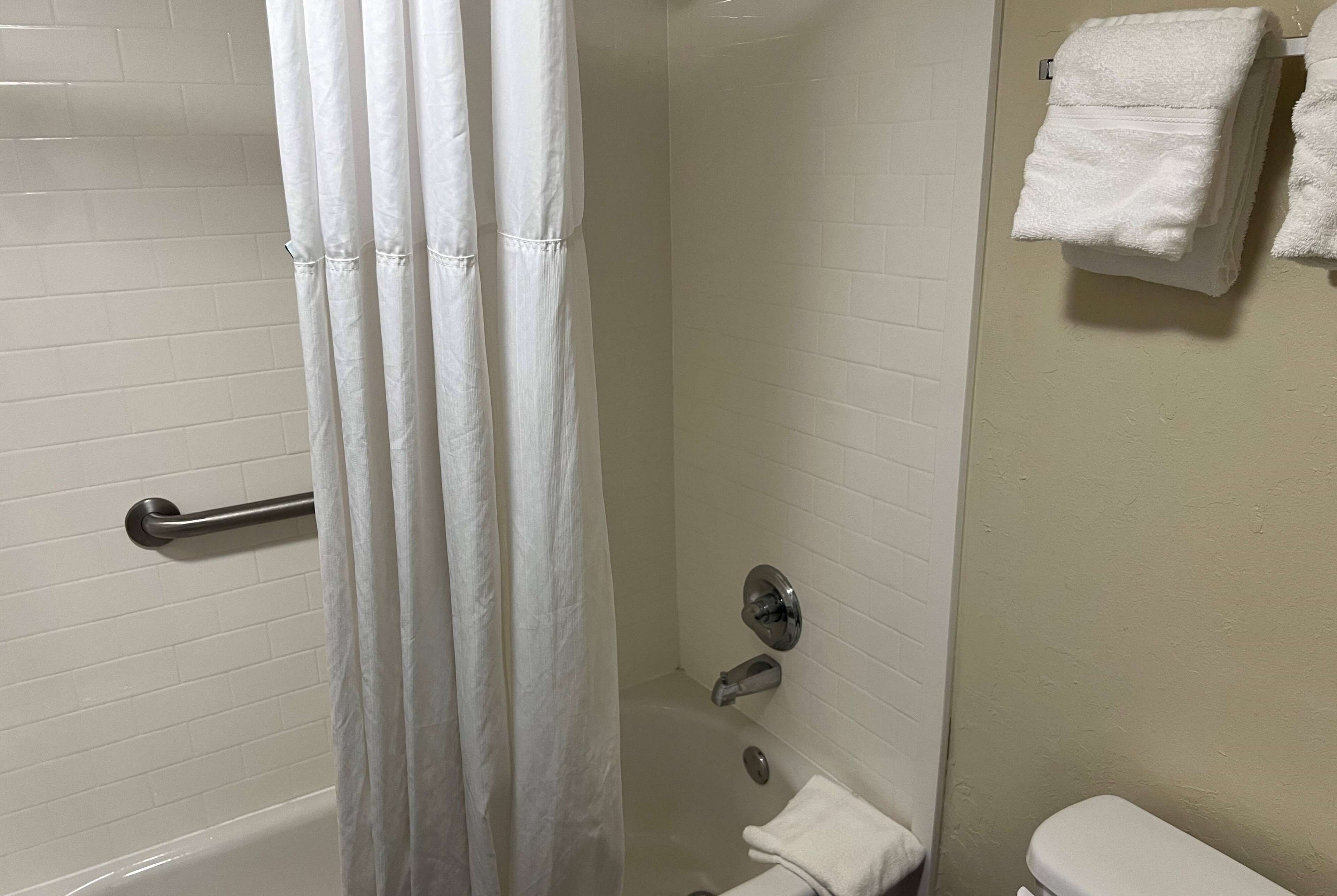 Ein Badezimmer mit einer Badewanne, einer Duschvorhang, einem Handtuchhalter mit Handtüchern und einer Toilette.