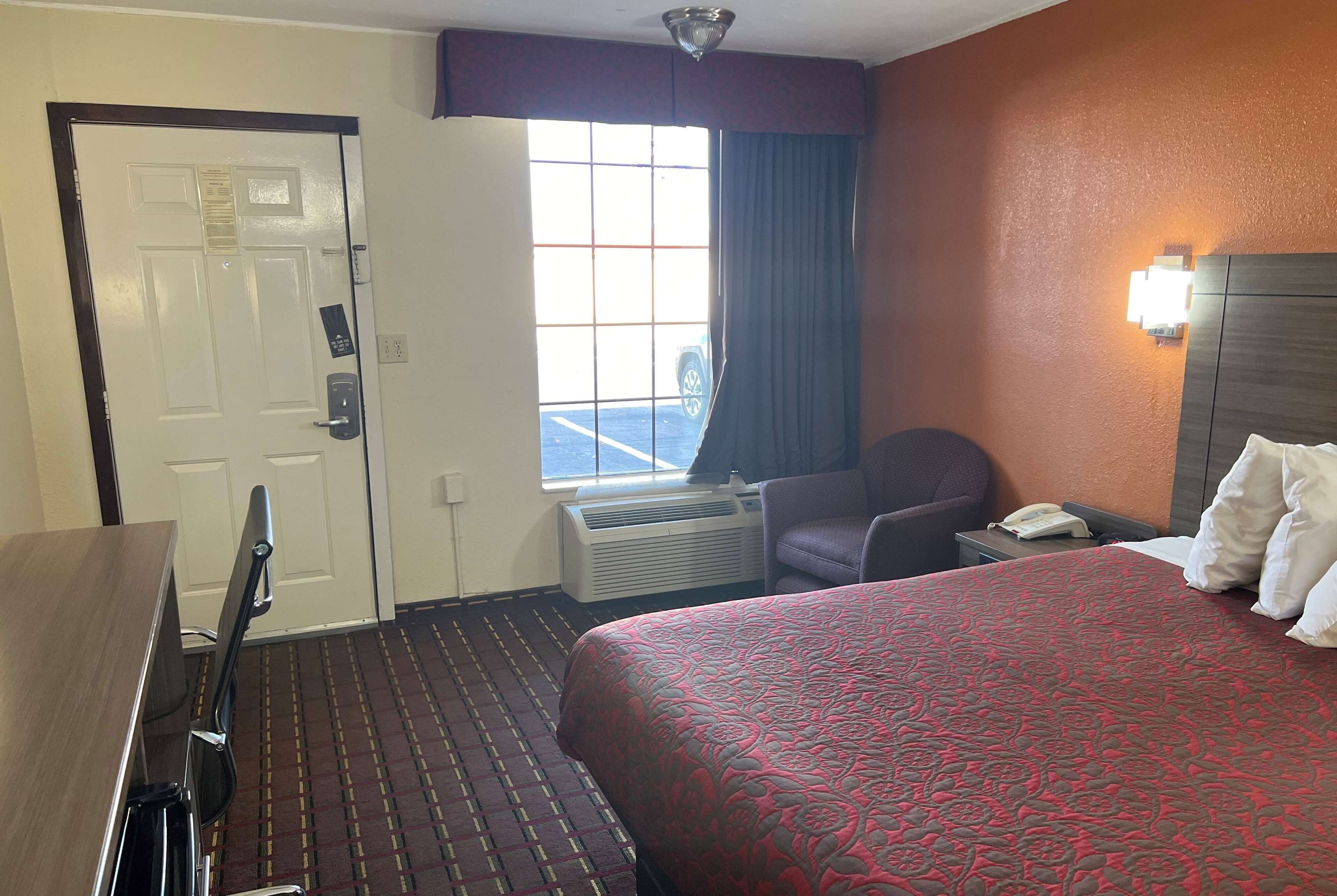 Ein Hotelzimmer mit Bett, Schreibtisch, Stuhl, Fenster mit Blick auf einen Parkplatz und einem an der Wand befestigten Telefon.