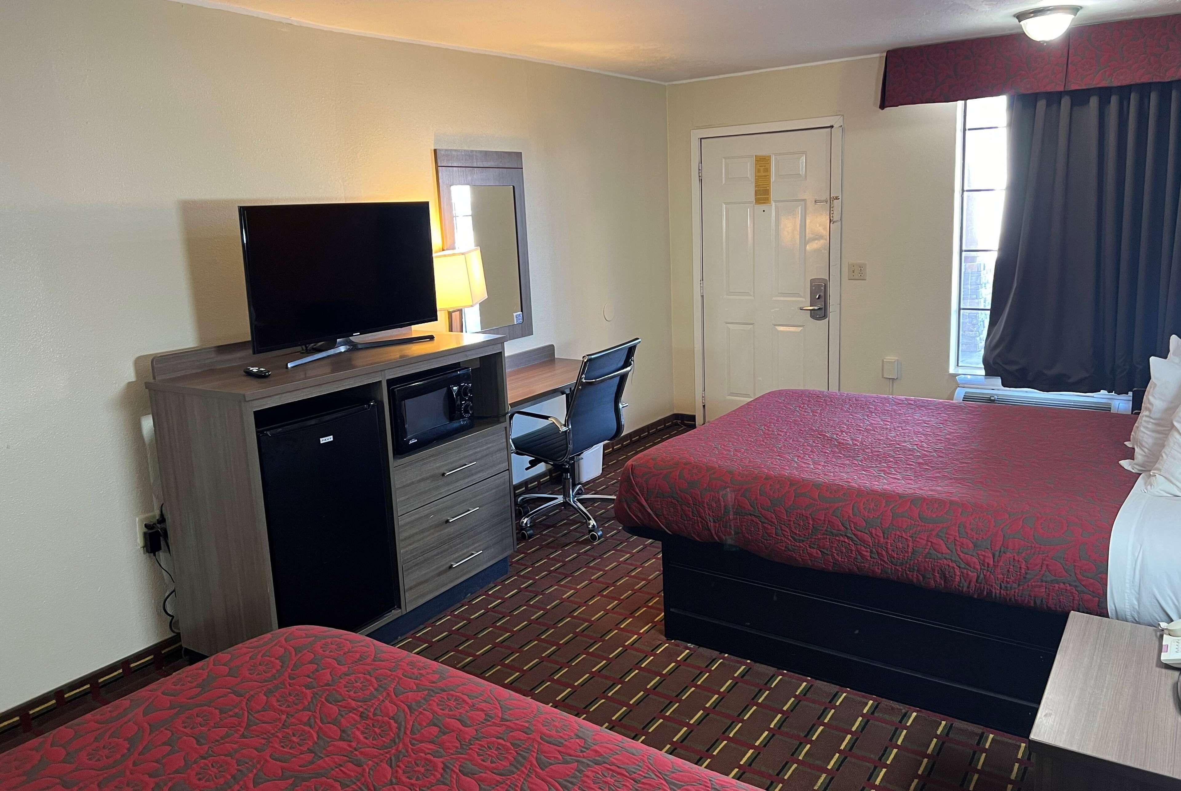 Une chambre d’hôtel avec deux lits, un bureau avec un ordinateur, une télévision et une porte.