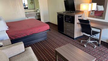A hotel room with a bed, a desk with a computer, a chair, a TV, and a lamp.