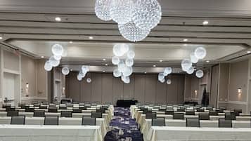 Une salle de conférence avec des rangées de tables et de chaises, un grand lustre et un pupitre à l’avant.