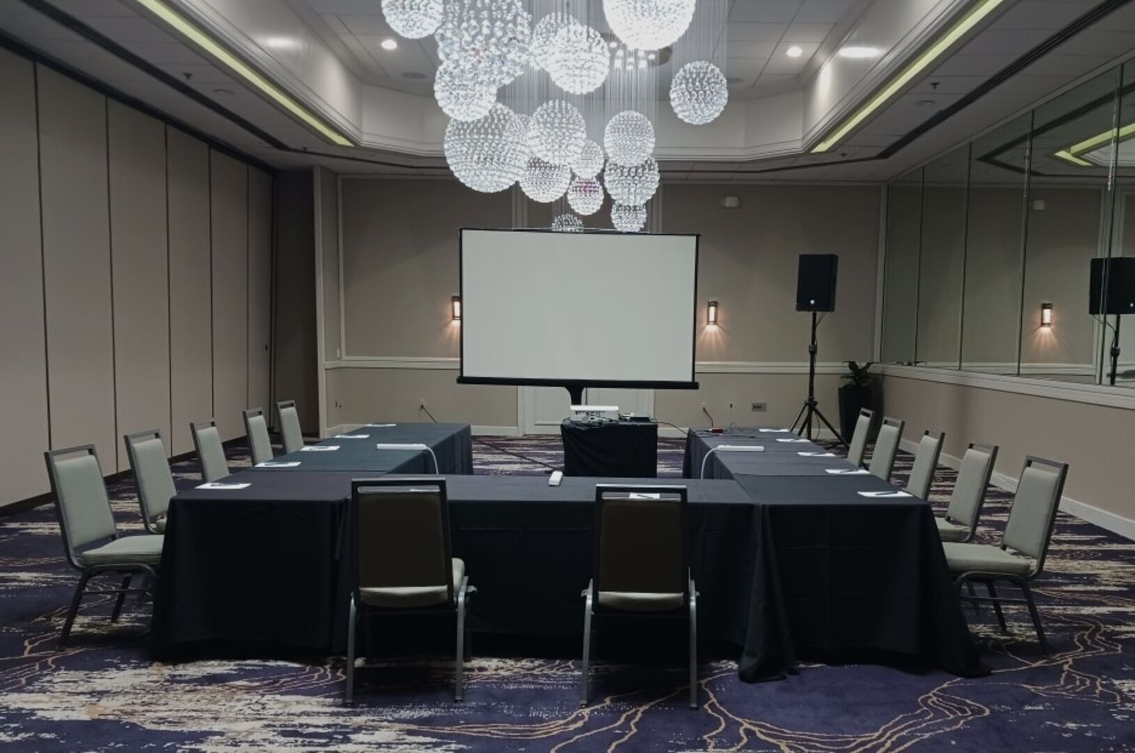 Un salón de conferencias con una gran mesa, sillas, una pantalla de proyector y una araña.