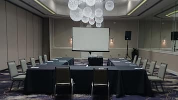 Un salón de conferencias con una gran mesa, sillas, una pantalla de proyector y una araña.