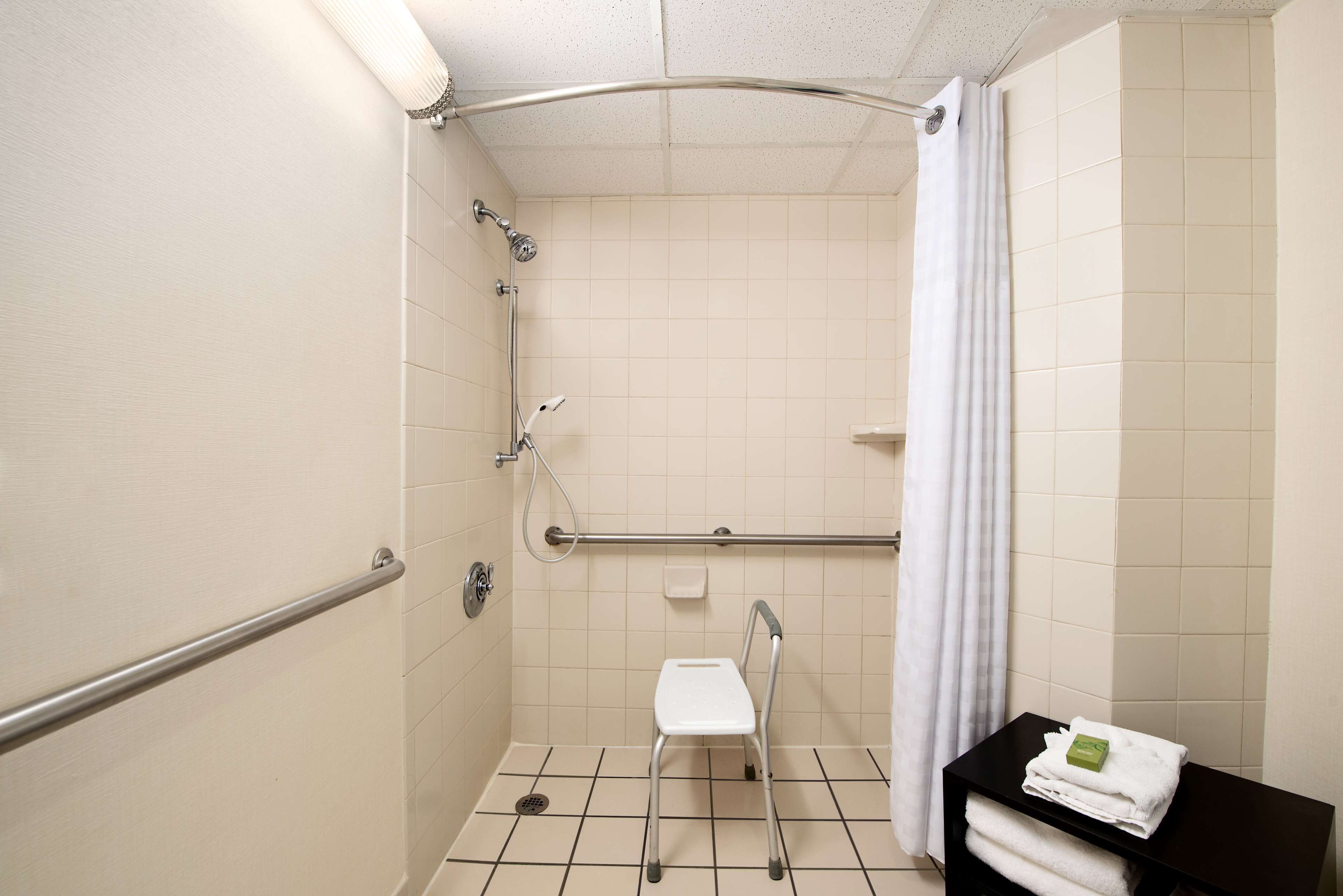 A small, tiled bathroom with a shower, a white chair, and a towel rack.