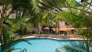 Piscina rodeada de palmeras y zonas de estar al aire libre con sombrillas.