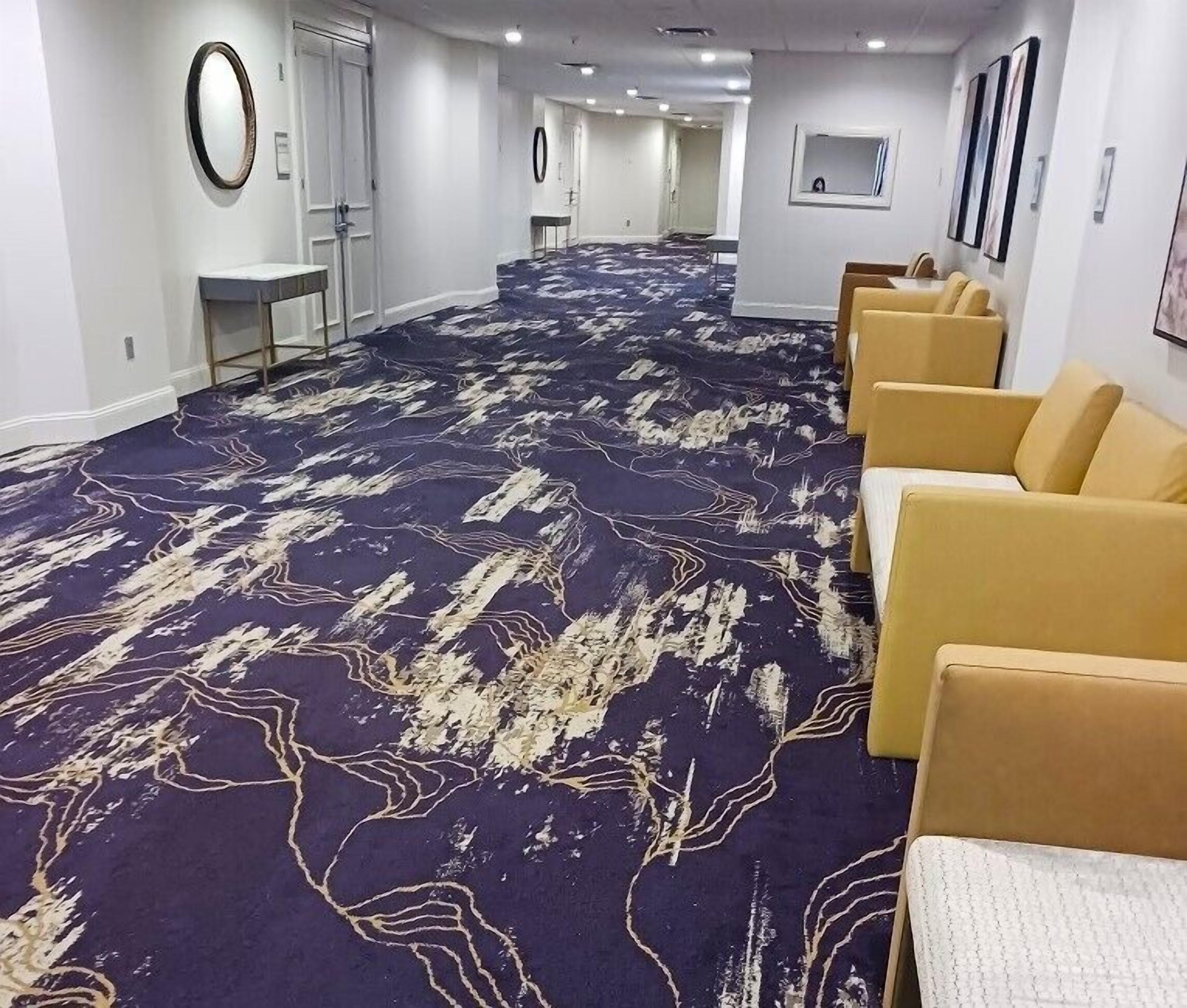 A hotel lobby with a patterned carpet, a reception desk, and seating area.