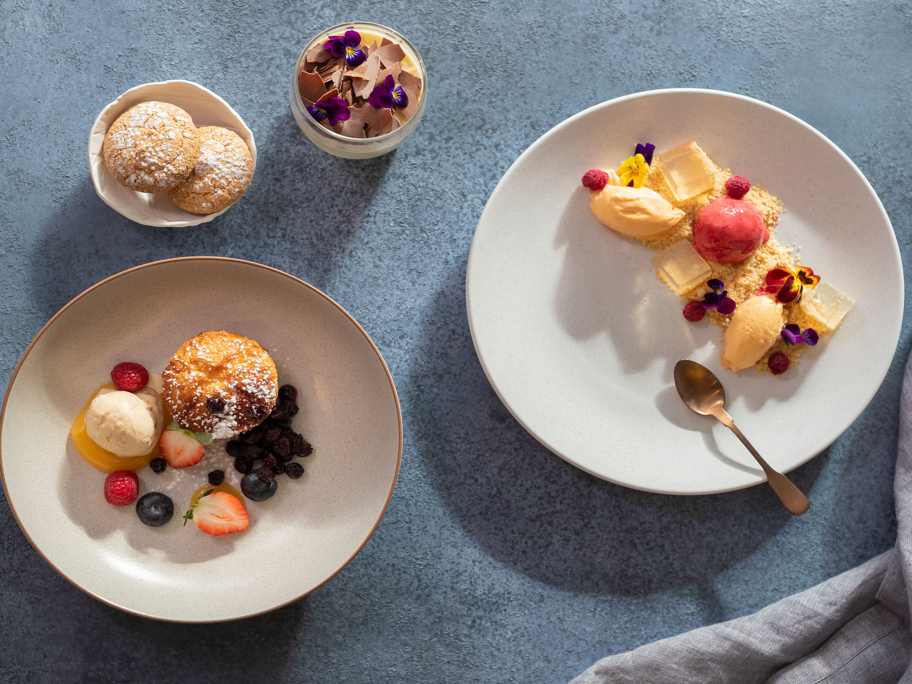 Two plates of desserts with various fruits and toppings, placed on a textured surface.