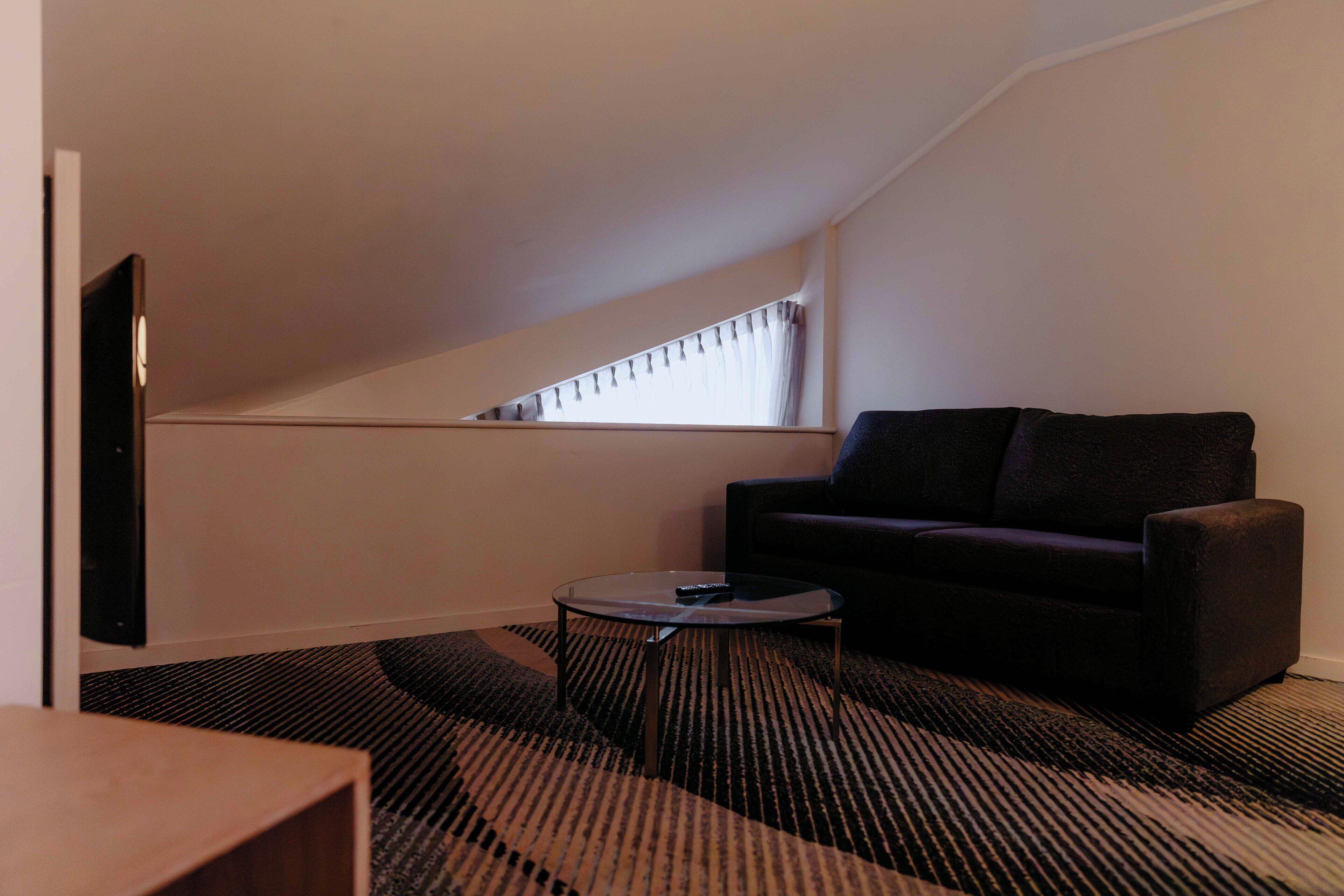 Una sala de estar moderna con un sofá oscuro, una mesa de centro de vidrio y un televisor de pantalla plana montado en la pared.