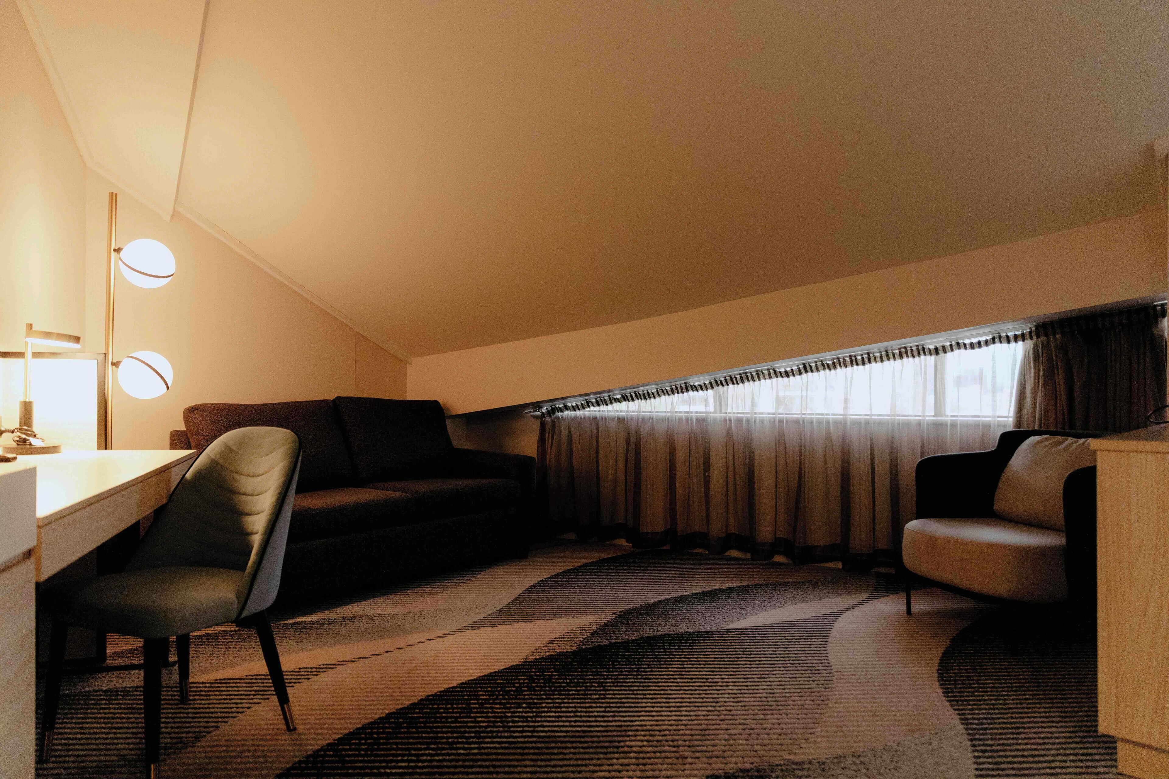 Une pièce confortable avec un bureau, deux chaises, un canapé et une grande fenêtre avec des rideaux.