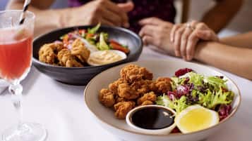 A dining table with a plate of fried chicken, a bowl of salad, and a glass of red drink.