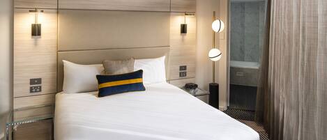 Quarto de hotel com uma cama grande, mesas de cabeceira, espelho e área de chuveiro.