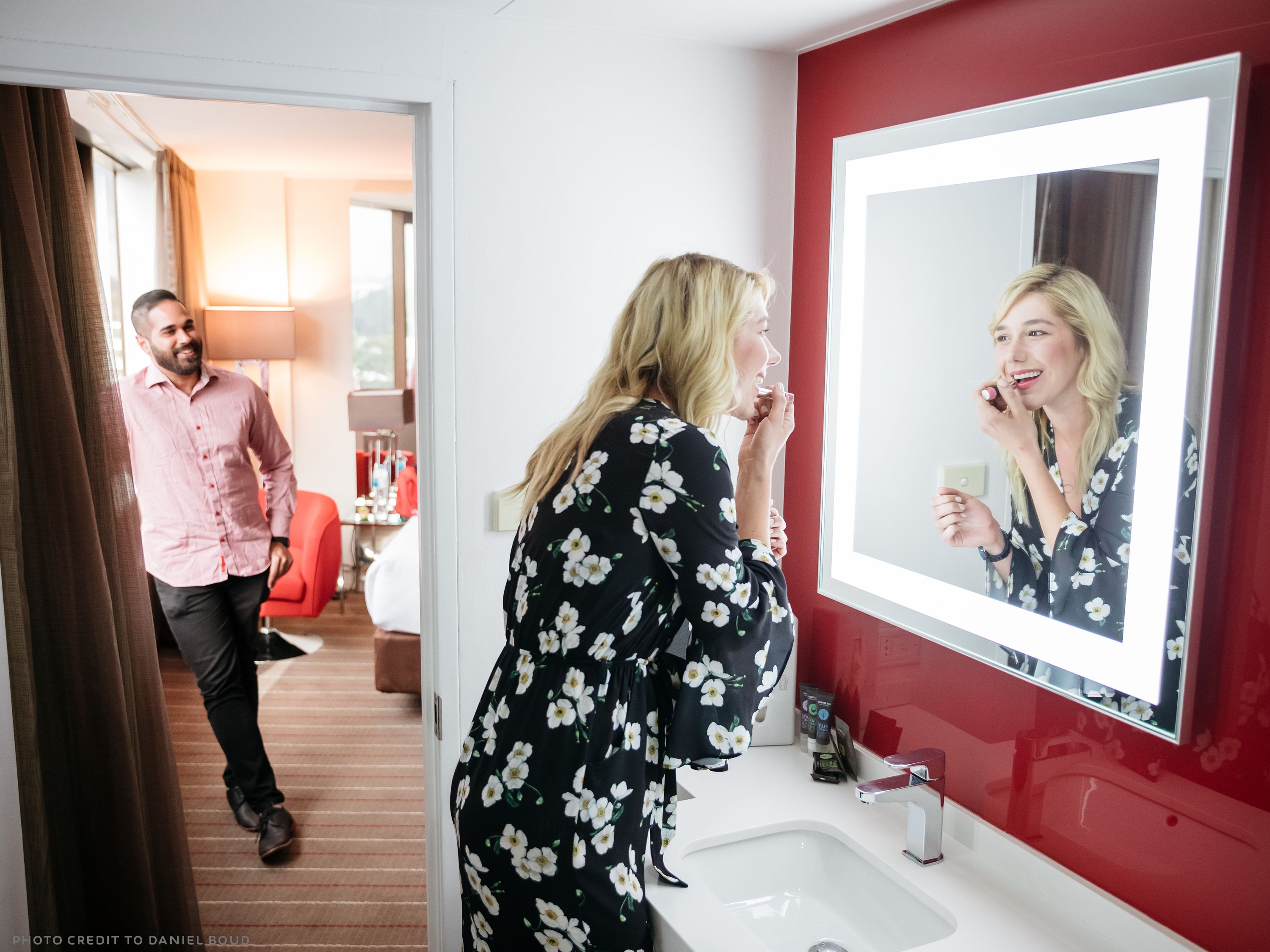 Une chambre d’hôtel avec un mur d’accent rouge, un grand miroir et un lavabo moderne.
