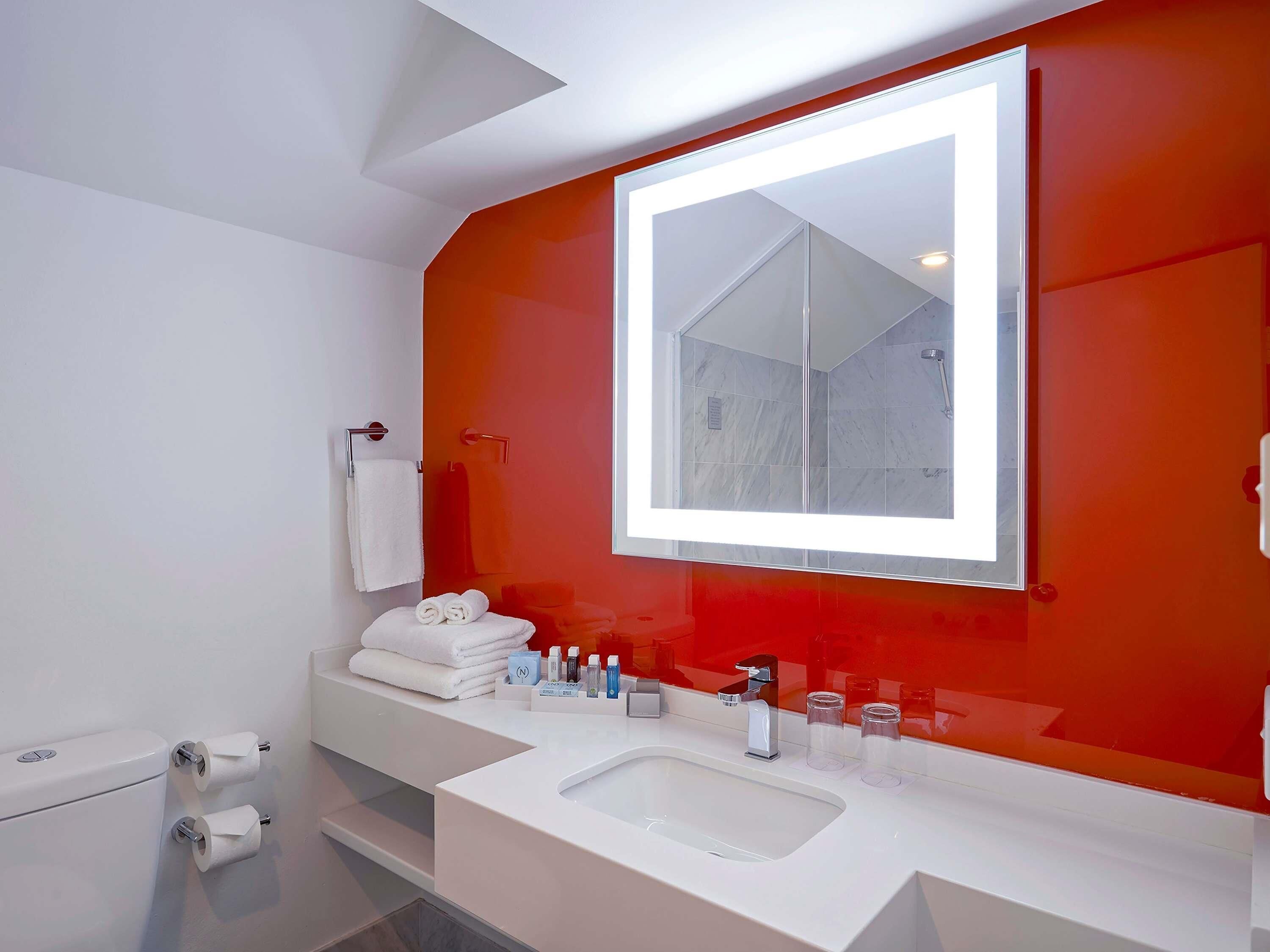A modern bathroom with a large mirror, white fixtures, and a red accent wall.