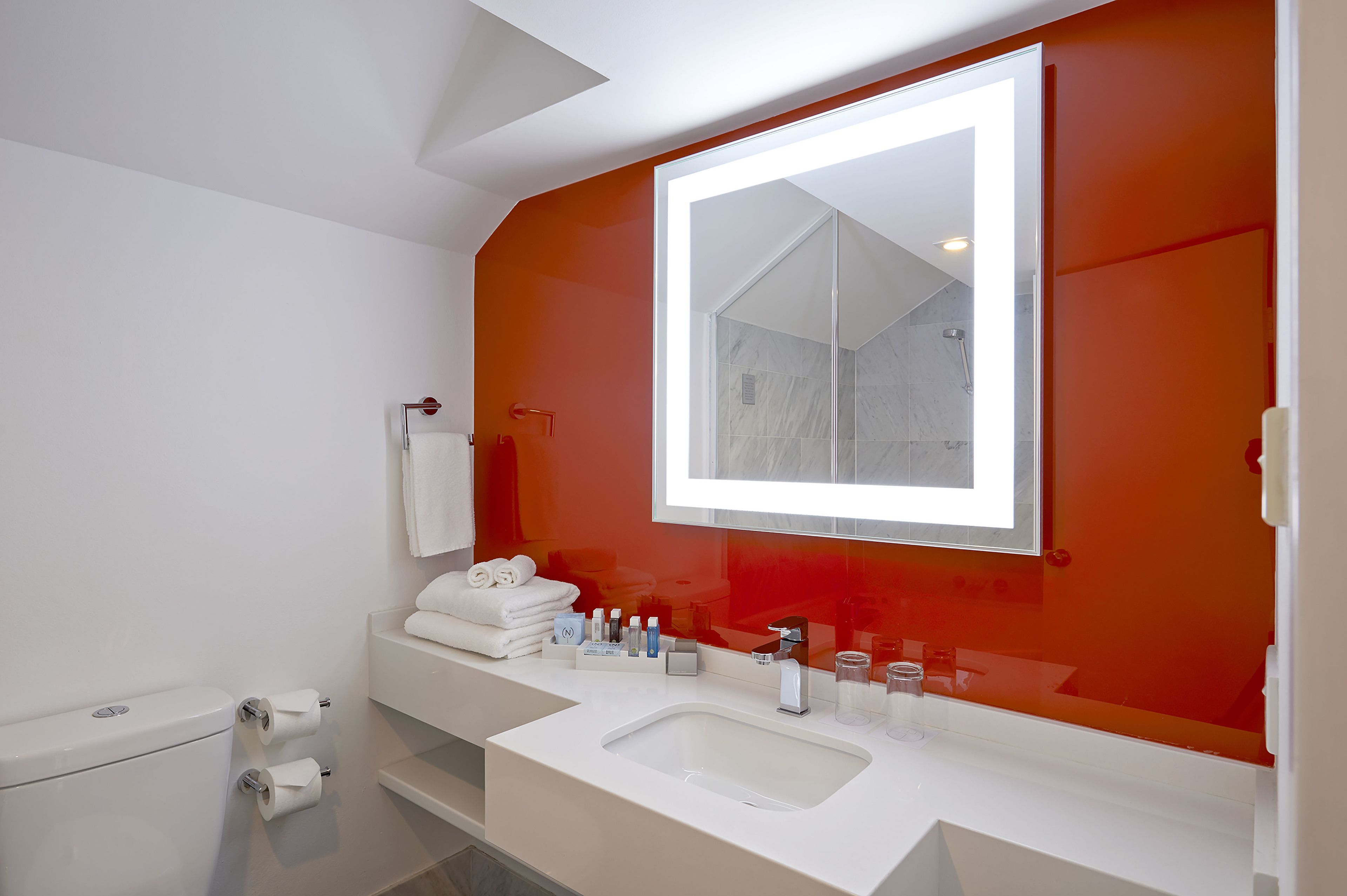 Un bagno moderno con uno specchio grande, sanitari bianchi e una parete rossa a contrasto.