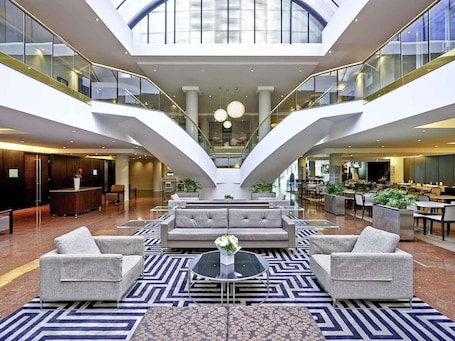 A spacious lobby with a central seating area, a reception desk, and a staircase leading to upper levels.. Novotel Sydney Parramatta