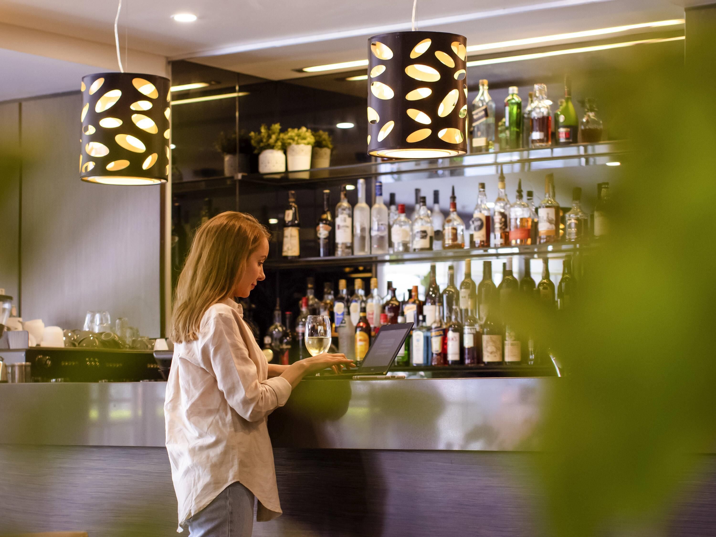 A person at a bar with a wine glass, shelves with bottles, and hanging pendant lights.
