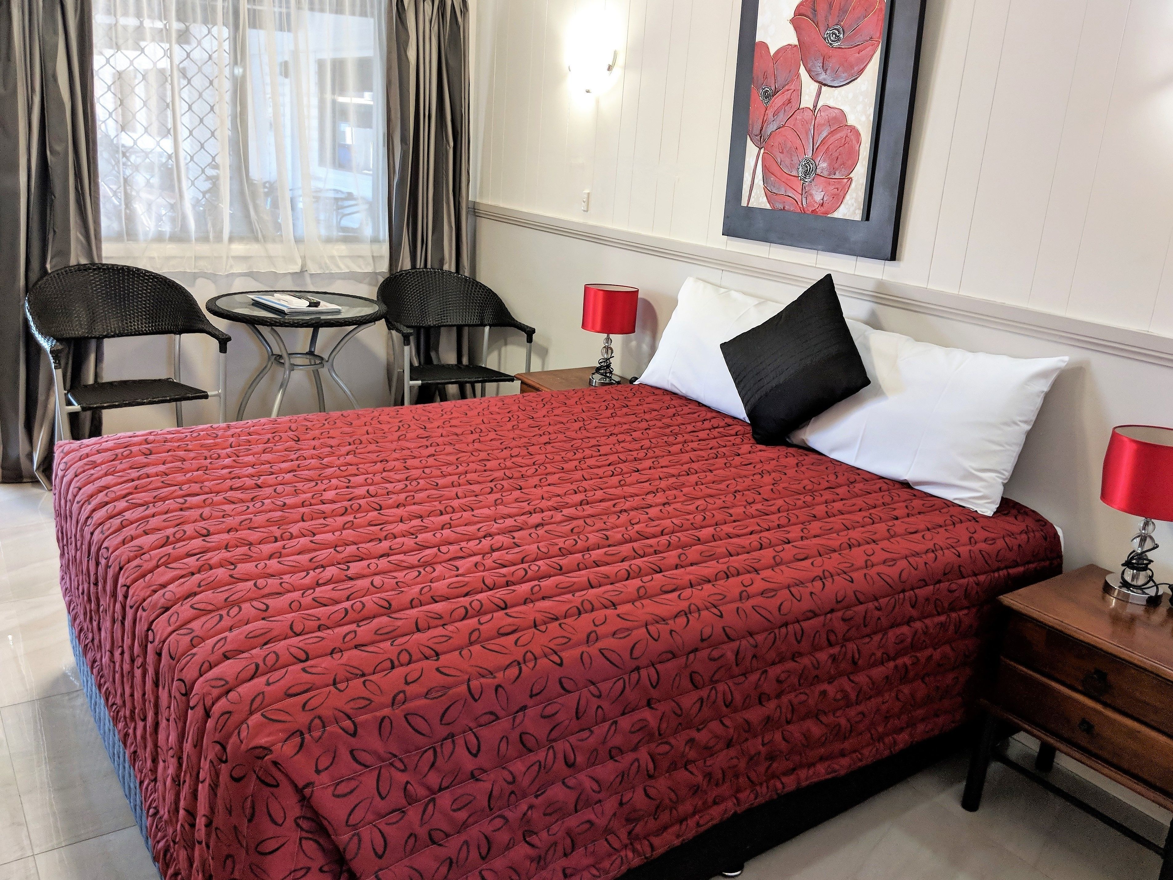 Ein Hotelzimmer mit einem großen Bett, zwei schwarzen Sesseln, einem kleinen Tisch und einer roten Lampe.