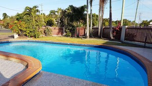 Una piscina con borde de ladrillo, rodeada por una zona de grava y una valla de madera.