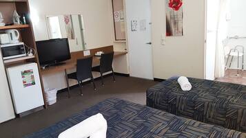 Une chambre d’hôtel avec deux lits, un bureau avec un ordinateur, une télévision et un four à micro-ondes.