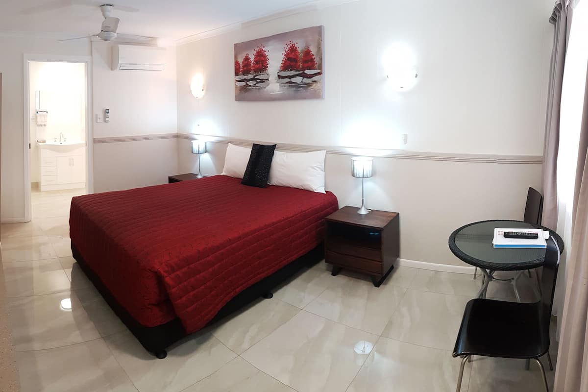 Quarto de hotel com uma cama, mesas de cabeceira, abajur, cadeira, televisão e um quadro na parede.