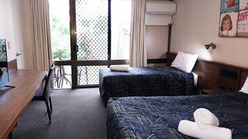 A hotel room with two beds, a desk, and a chair. There is a window with curtains and an air conditioning unit on the wall.