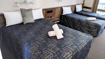 A hotel room with two beds, each with a patterned bedspread and pillows. There is a small shelf with toiletries and a clock on the wall.