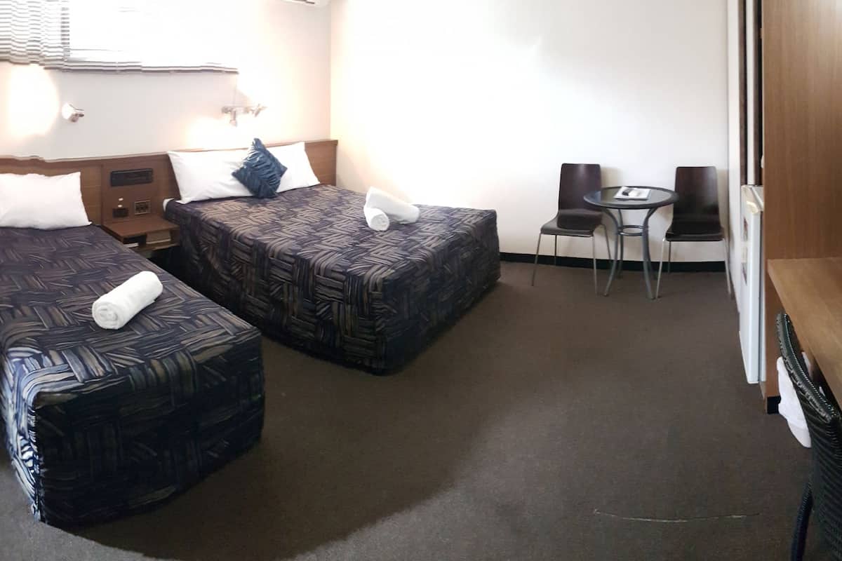 Quarto de hotel com duas camas, uma mesa pequena, duas cadeiras, televisão e um mini-bar.
