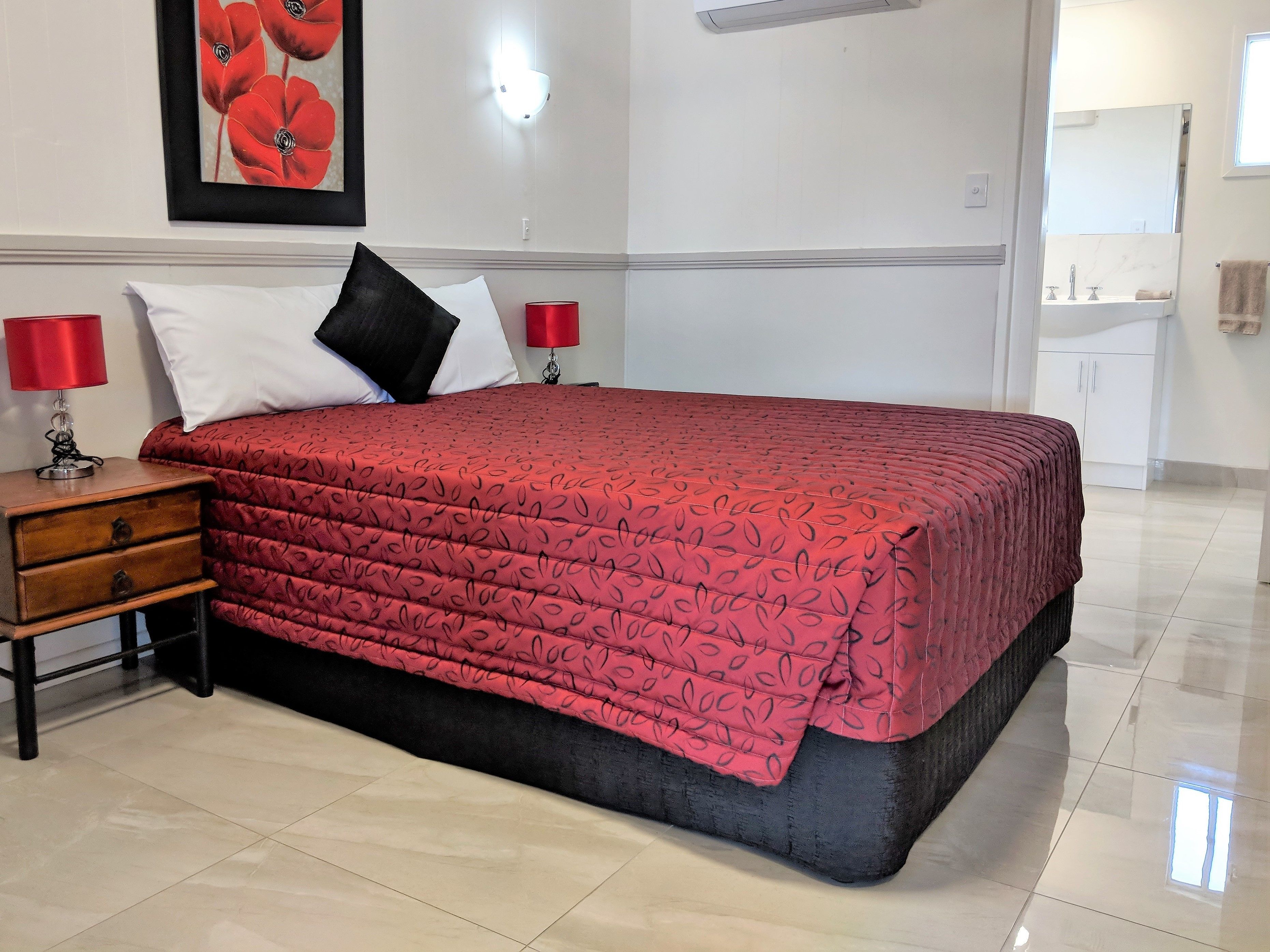 A neatly made bed with a patterned bedspread, a nightstand with a lamp, and a framed picture on the wall.