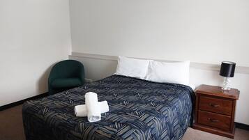 A hotel room with a bed, a chair, a nightstand with a lamp, and a towel on the bed.