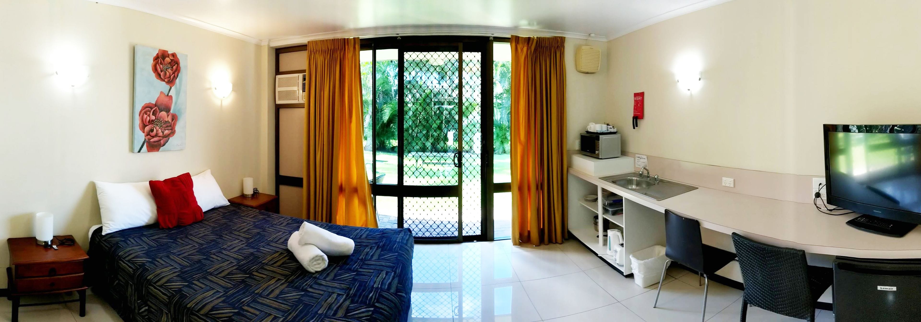 A hotel room with a bed, a desk, a television, and a view of the outdoors.