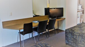Una habitación pequeña y funcional con una cama individual, un escritorio con dos sillas, un televisor y un microondas.