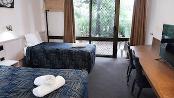 Habitación de hotel con dos camas, un escritorio, un televisor y un balcón con vistas a zonas verdes.